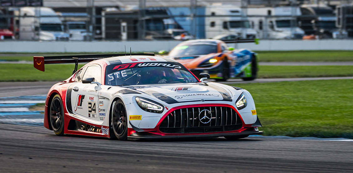 A red and white Mercedes-AMG GT3 racing car with start number 34 drives on a racetrack while another vehicle follows in the background.